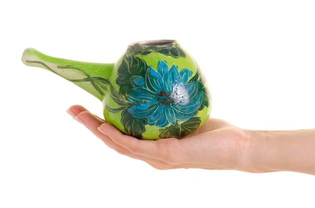 keramická konvička na proplach nosu zelené barvy s malovaným květem položená na ruce